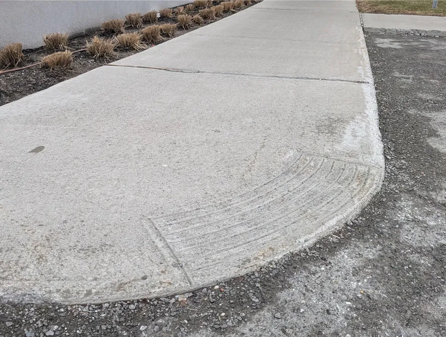 Trottoir en béton avec bordure abaissée en pente douce facilitant la transition vers la chaussée, avec une surface texturée permettant une détection au pied ou à la canne.