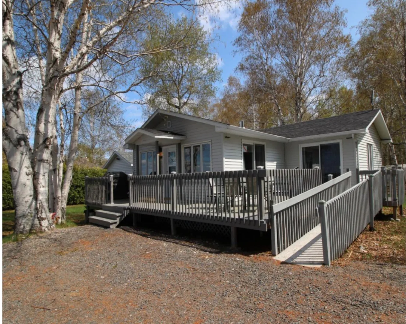 Chalet accessible avec rampe et terrasse clôturée, entouré d’arbres en automne. Accès facile et stationnement proche.