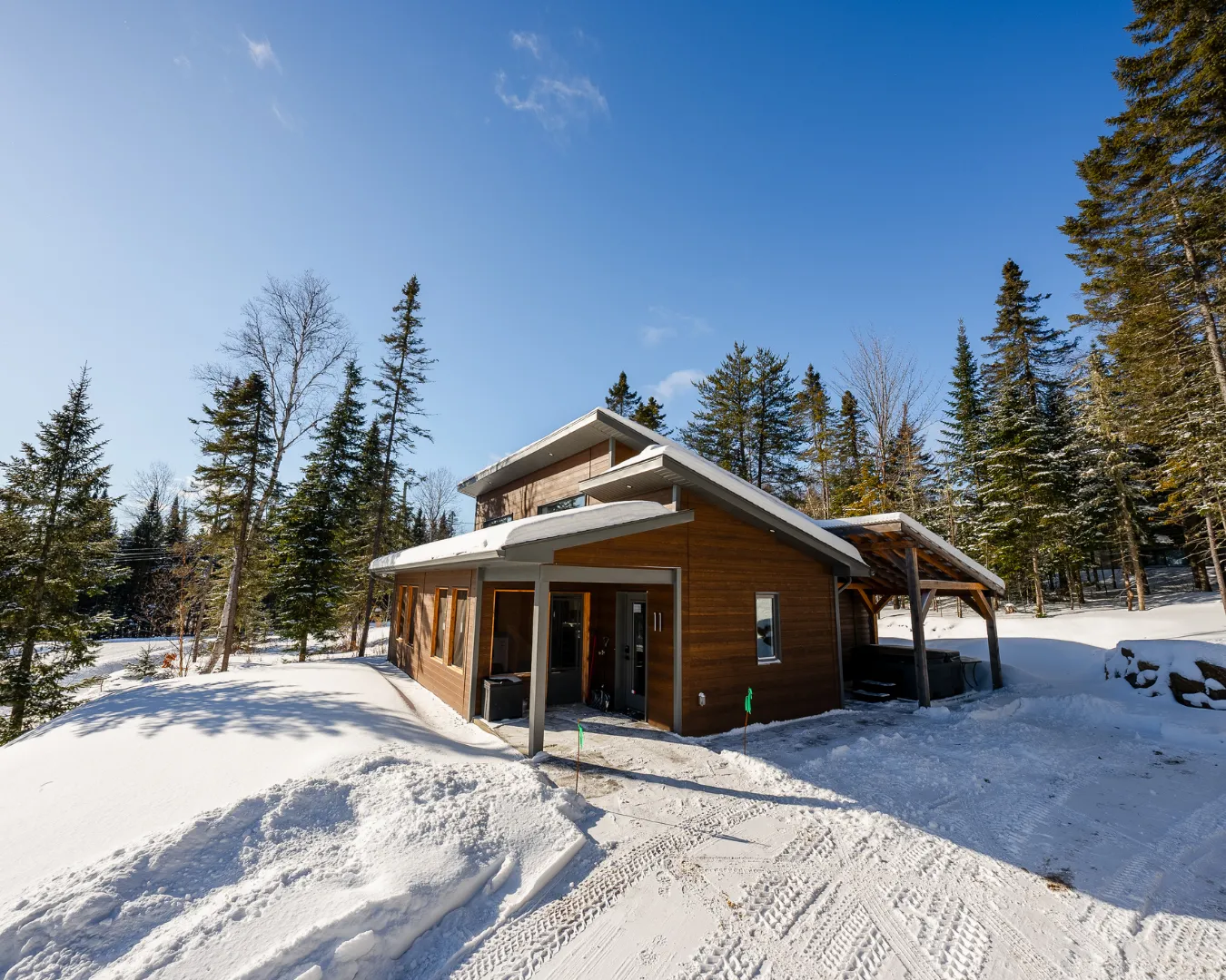 Chalet contemporain en hiver entouré de neige et forêt. Accès dégagé avec entrée couverte et stationnement.