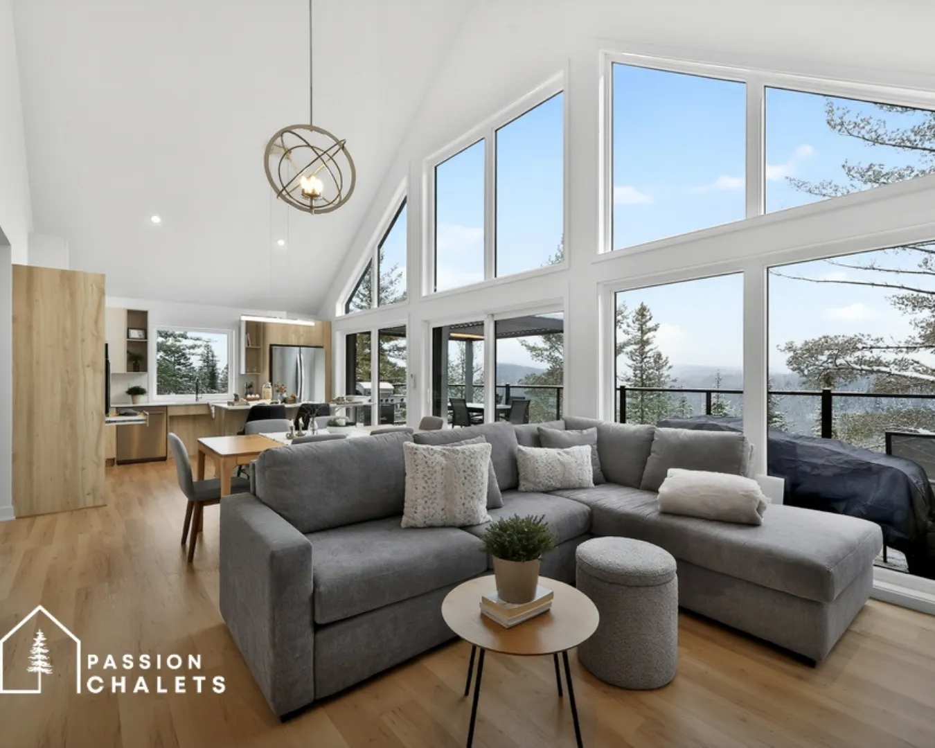 Salon moderne avec grandes fenêtres panoramiques et vue nature. Espace ouvert avec canapé et cuisine intégrée.