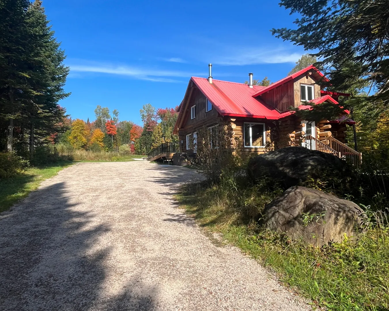 Chalet en bois avec toit rouge près d’un chemin forestier. Environnement naturel avec arbres colorés en automne.