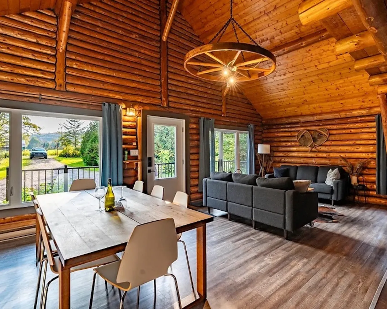 Intérieur de chalet en bois avec salon ouvert et grande table à manger. Espace lumineux et convivial avec grandes fenêtres.
