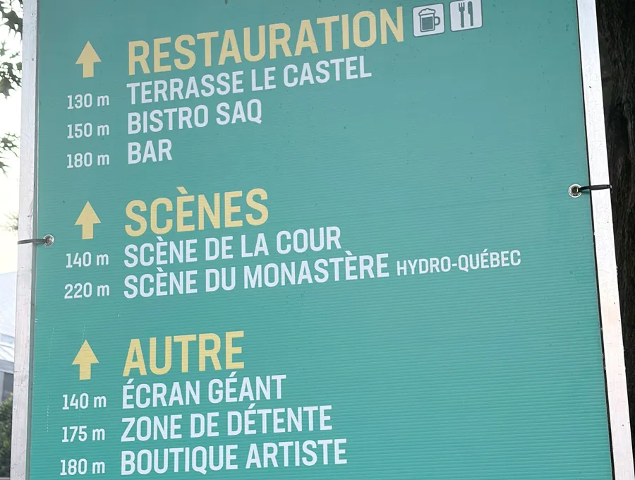 Panneau de signalisation du FestiVoix indiquant les distances en mètres vers les zones de restauration, les scènes, l’écran géant, la zone de détente et la boutique artiste.