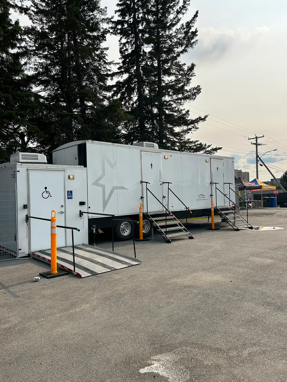 Roulotte sanitaire extérieure avec une entrée accessible par une rampe et plusieurs autres entrées munies d’escaliers.