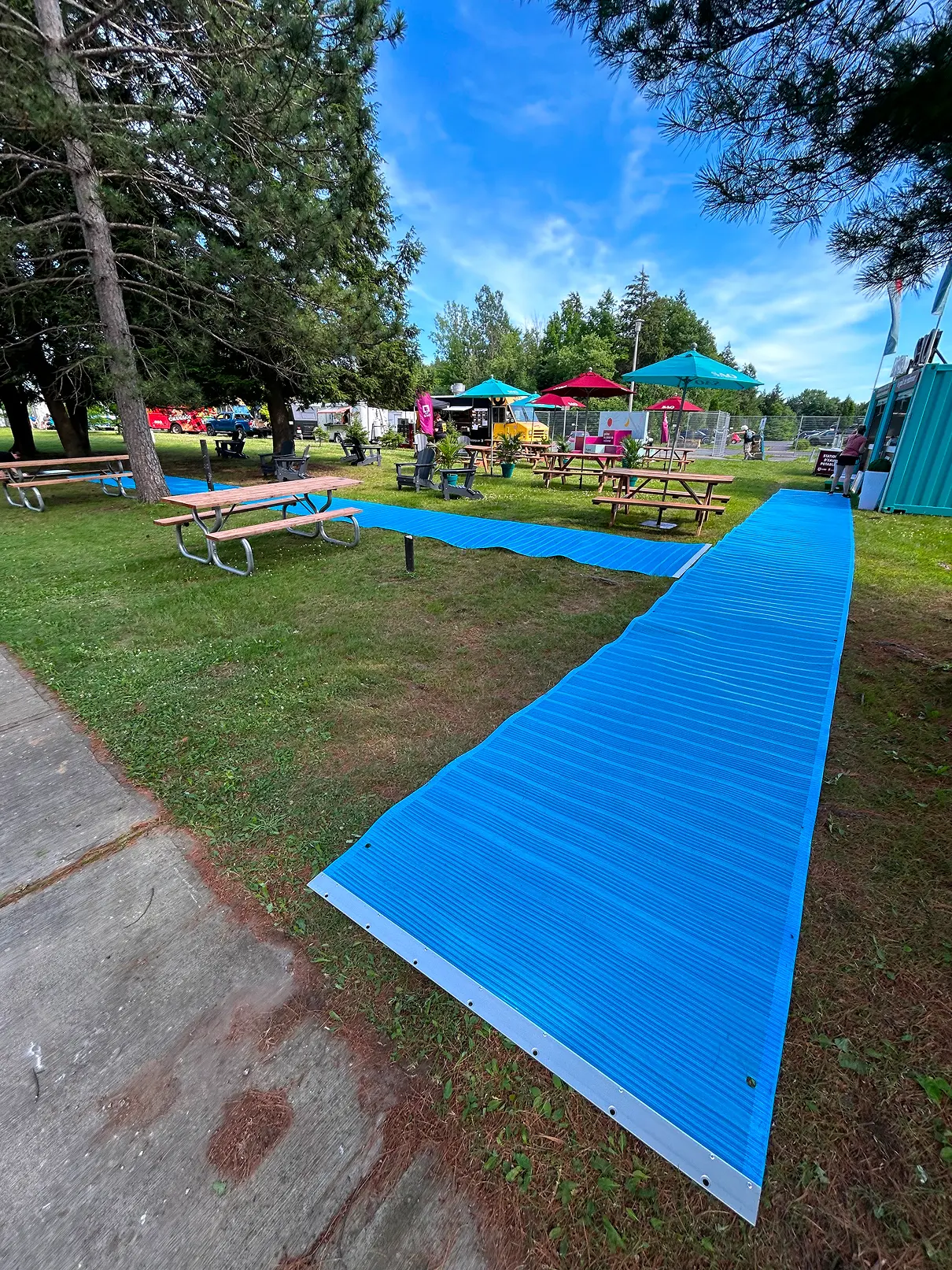 Tapis bleu déployé sur le gazon pour créer un cheminement stable entre une allée et les installations du festival.