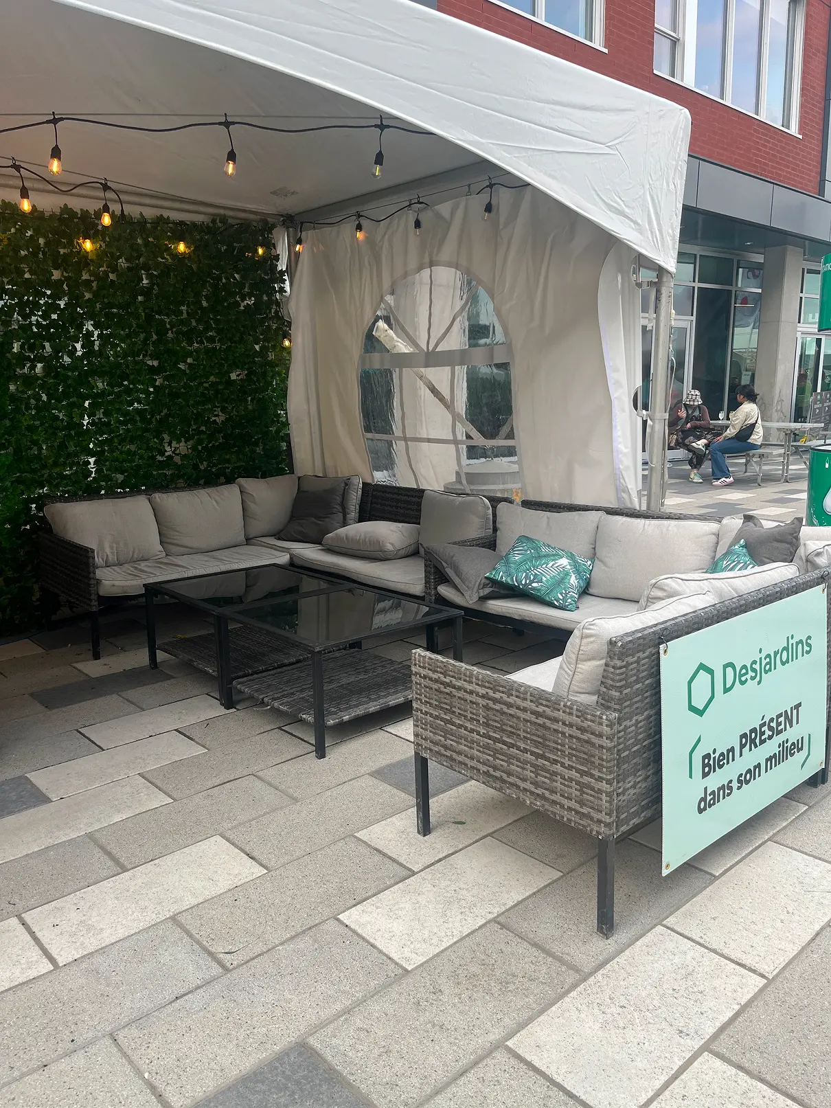 Espace de repos sous une tente, avec divans rembourrés, coussins et tables basses sur une surface pavée.