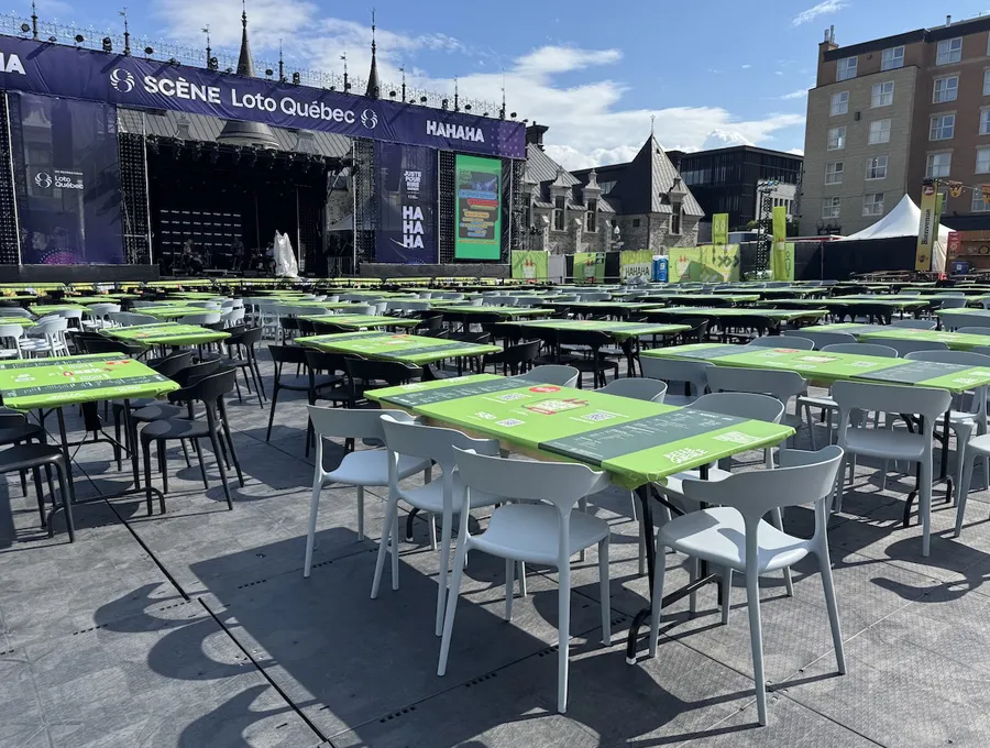 Grande zone de tables et de chaises installée devant une scène extérieure de festival, sur un revêtement stable et uniforme.