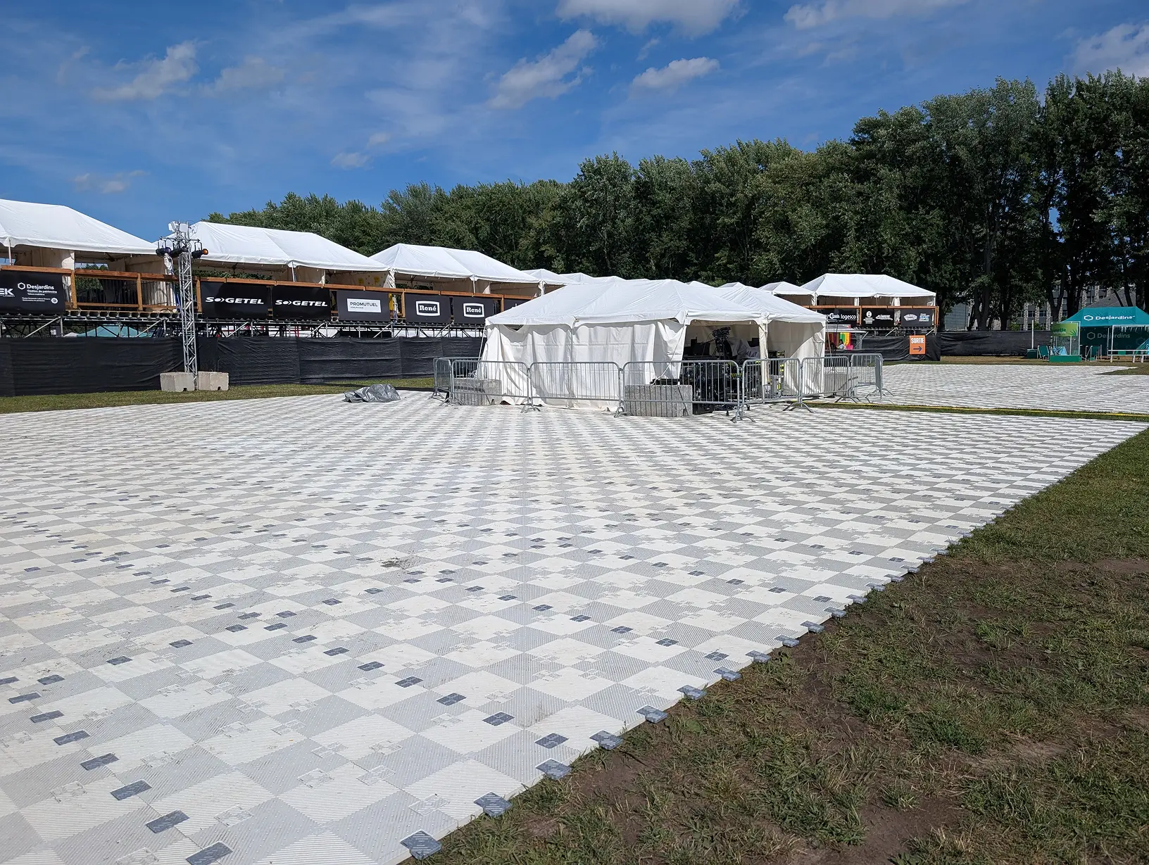 Grande surface temporaire en dalles modulaires installée sur le gazon devant des tentes et des installations de festival.