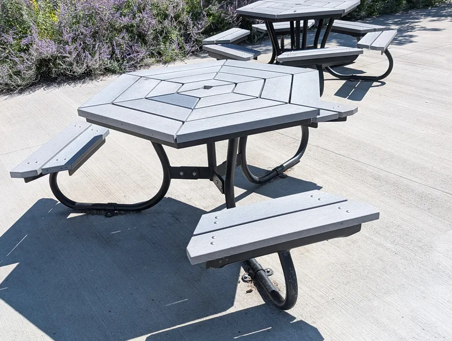 Table de pique-nique polygonale avec plusieurs bancs séparés, installée sur une surface dure et uniforme.
